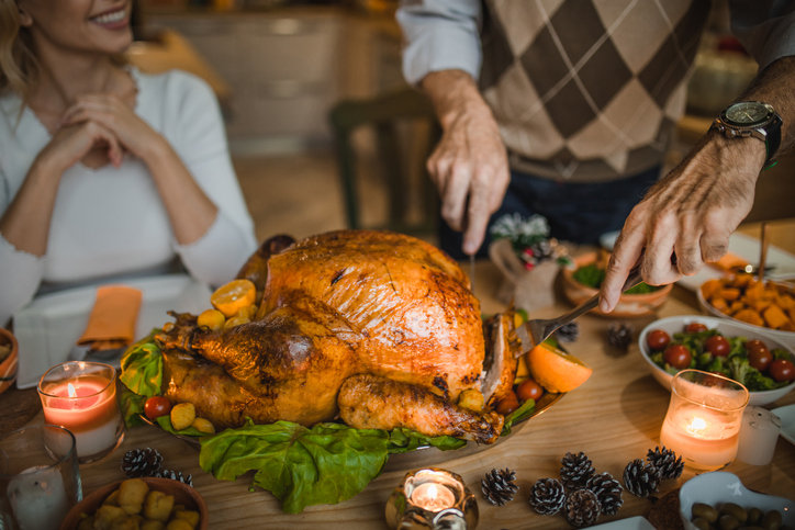 Unrecognizable person carving roasted turkey during Thanksgiving dinner at dining table.